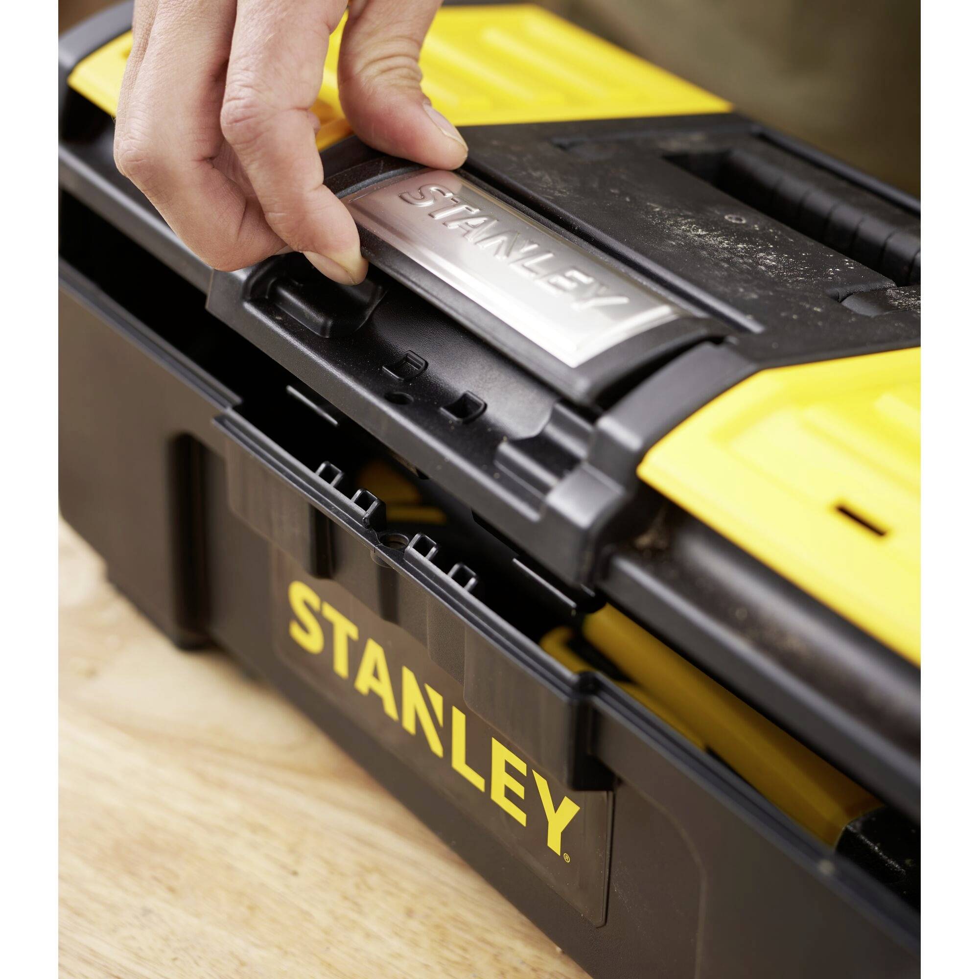 A hand opens a yellow and black Stanley toolbox.