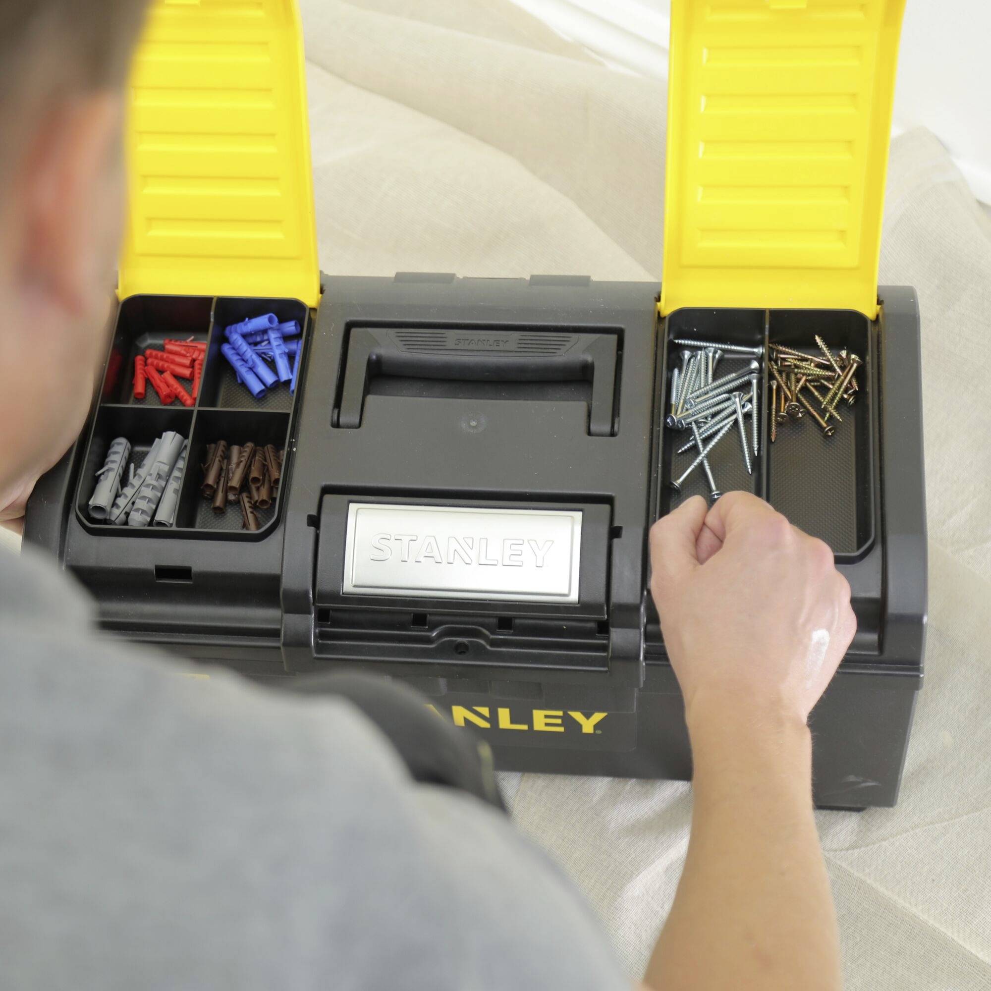 A person is looking at an open toolbox with various screws and wall plugs in separate compartments.