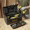 A person is holding a drill near an open toolbox with several Stanley power tools on a wooden table.