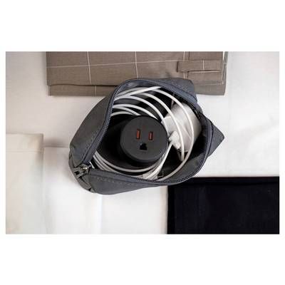 Open black zip pouch holding a coiled white power cable and black electrical outlet adapter on a bed or table.