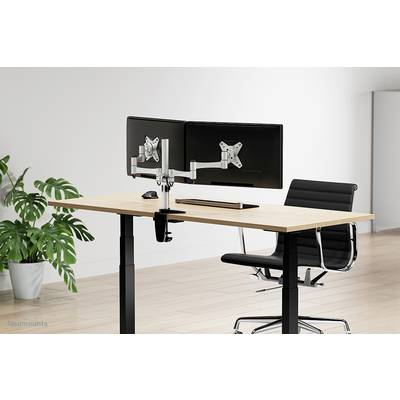Modern desk with two monitors, adjustable mount and ergonomic chair, on a light wooden floor. Plant in the background.