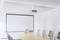 Conference room with a large projector screen, long wooden table and several chairs. Bright, minimalist interior design.