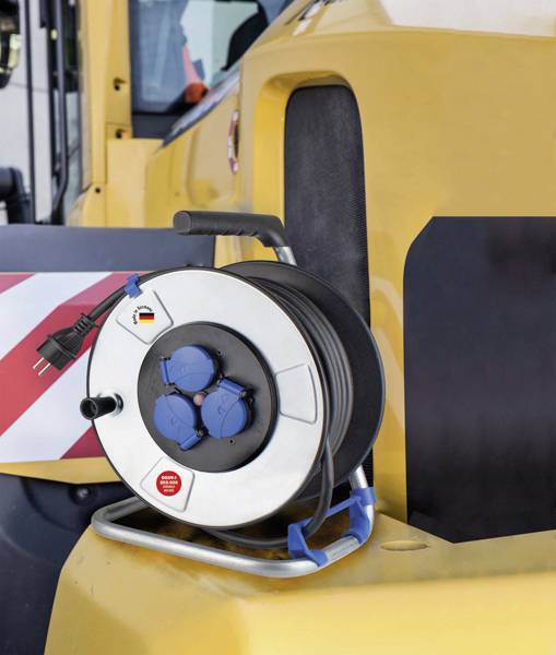 A cable reel with three blue sockets and a German plug is lying on a yellow vehicle, possibly for construction site requirements.