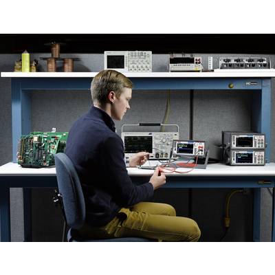 A person is working at a desk with electronic devices such as oscilloscopes and circuit boards. They are holding a clamp.