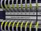 Network cabling with numbered grey cables in a server rack. Yellow labels facilitate port identification.