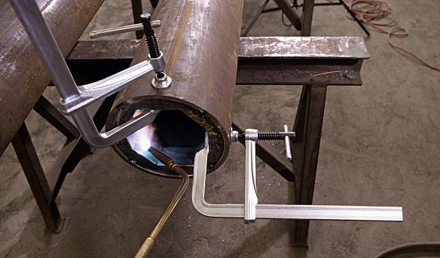 A metal tube is secured with several clamps while an internal welding process is carried out using an acetylene torch.
