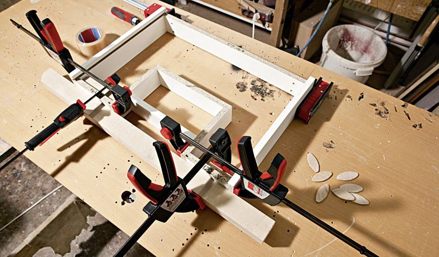 Woodworking on a table with clamps, wooden planks and connecting elements in the workshop. A wooden frame structure is being secured.