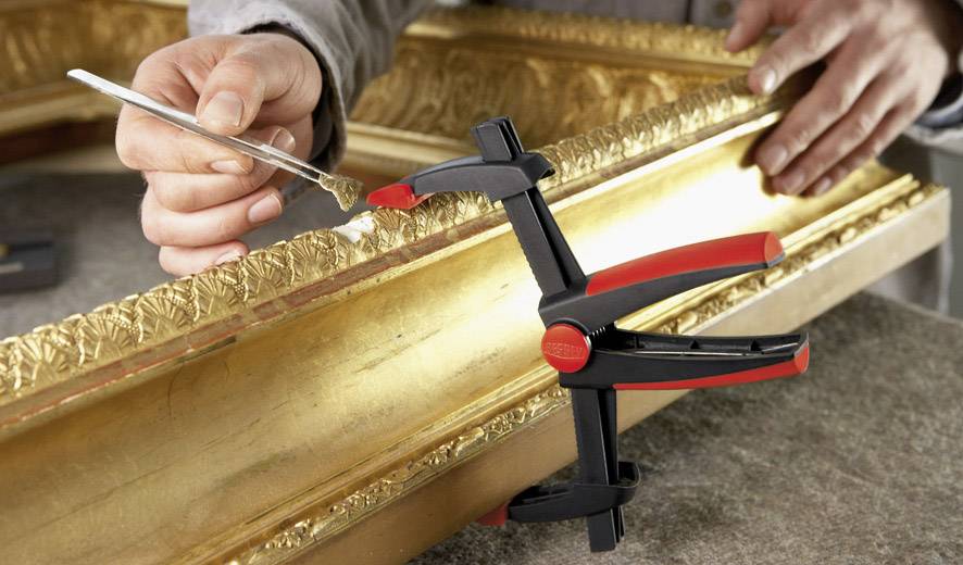 A person is restoring a gilded picture frame by repairing details with a small tool.