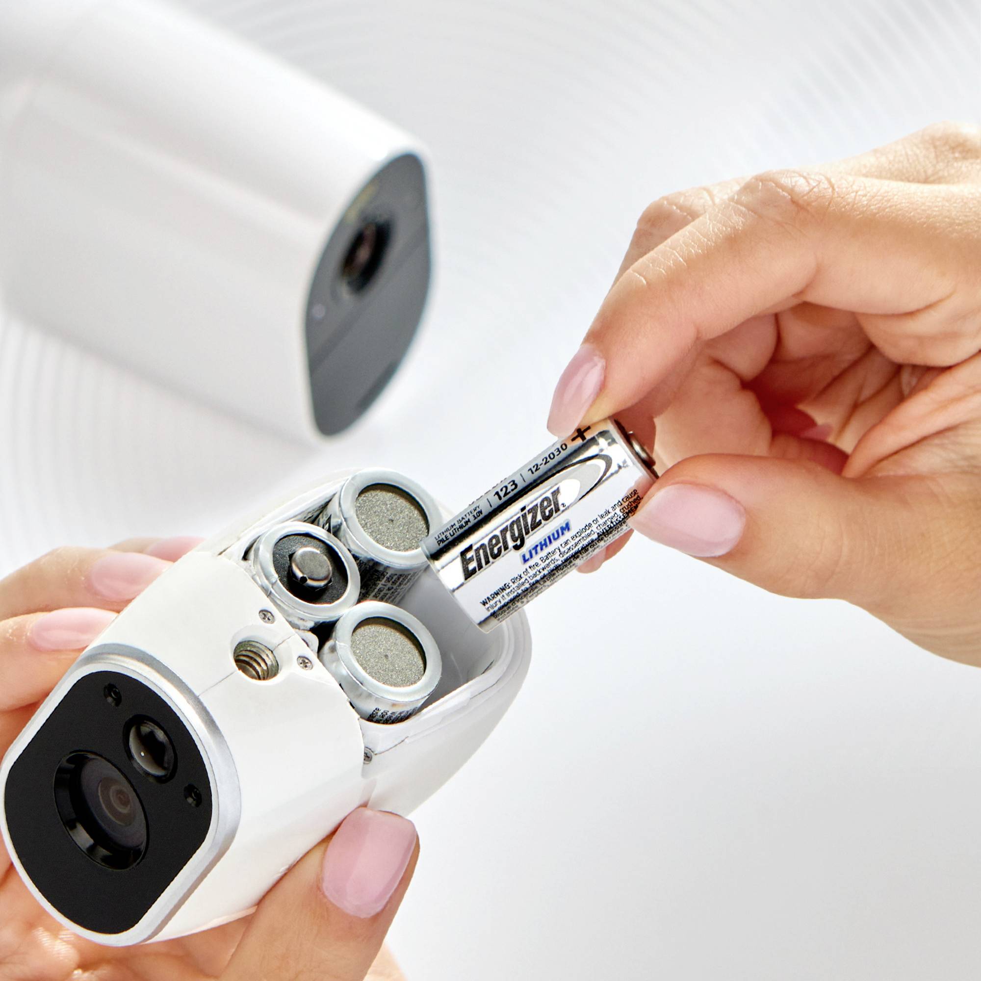 A hand is inserting a battery into a white, cylindrical camera lying on a table.