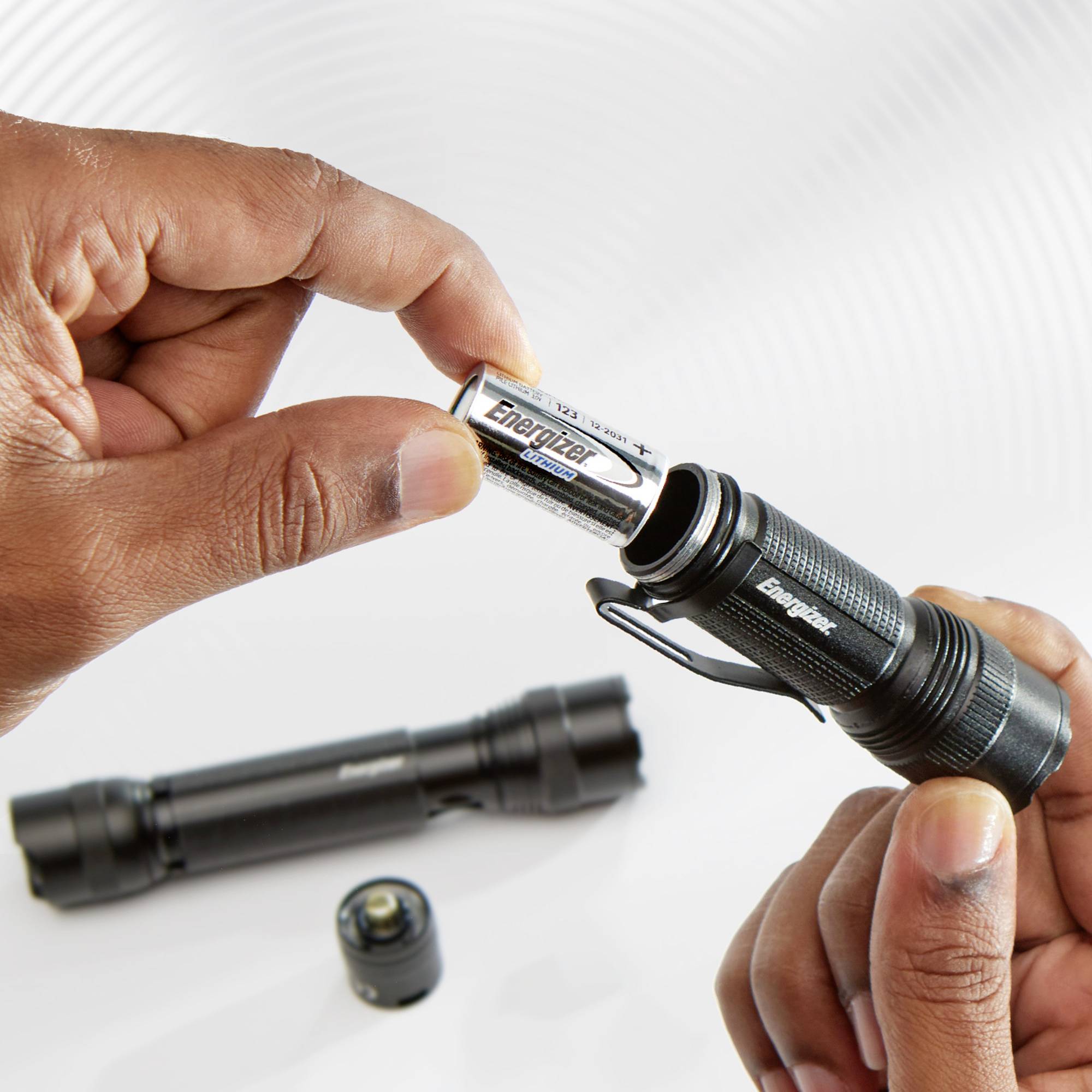 Two hands are holding a torch and a battery being inserted. A second torch and battery are lying in the background.