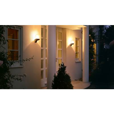 Entrance area of a house with illuminated wall lights, two large columns, and a glazed door, surrounded by plants.