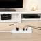 Multiple socket extension lead on a table, filled with various chargers and cables, in front of a television and shelves in the background.