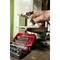 A hand adjusts a metal drill bit on a machine, close to an open red toolbox containing various metal attachments.