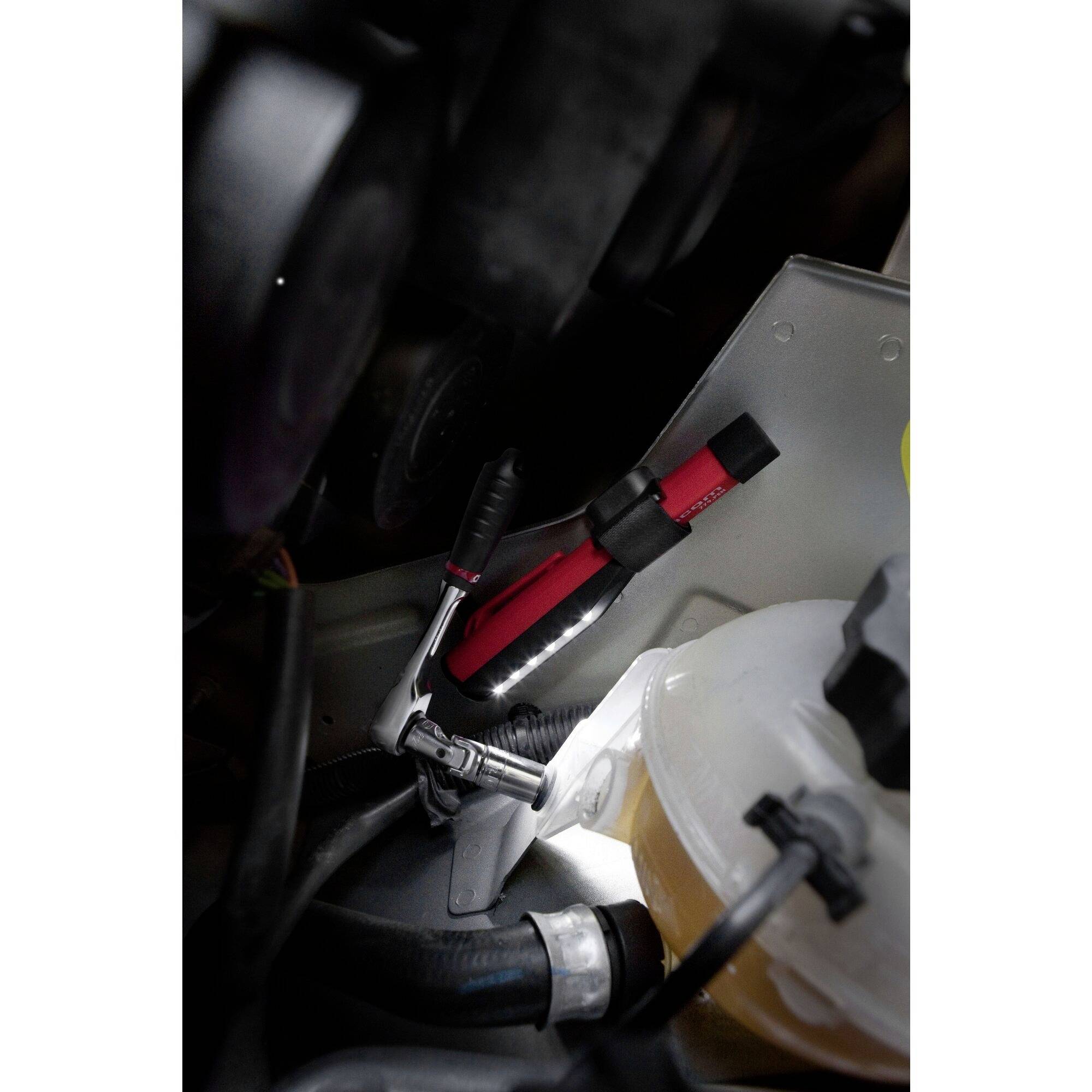 A spanner and a pair of pliers are lying in an engine bay next to a transparent fluid container.