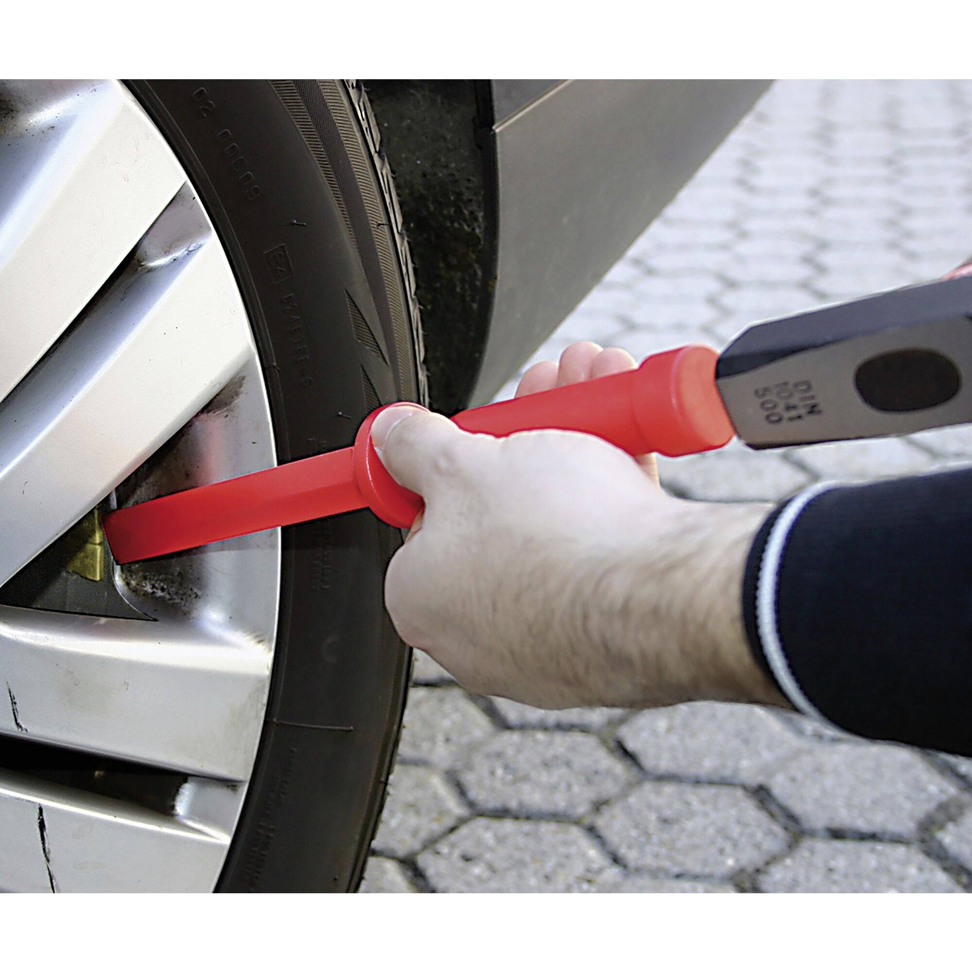 A person is repairing the aluminium spokes of a silver car tyre with a tool in their hand on cobblestones.