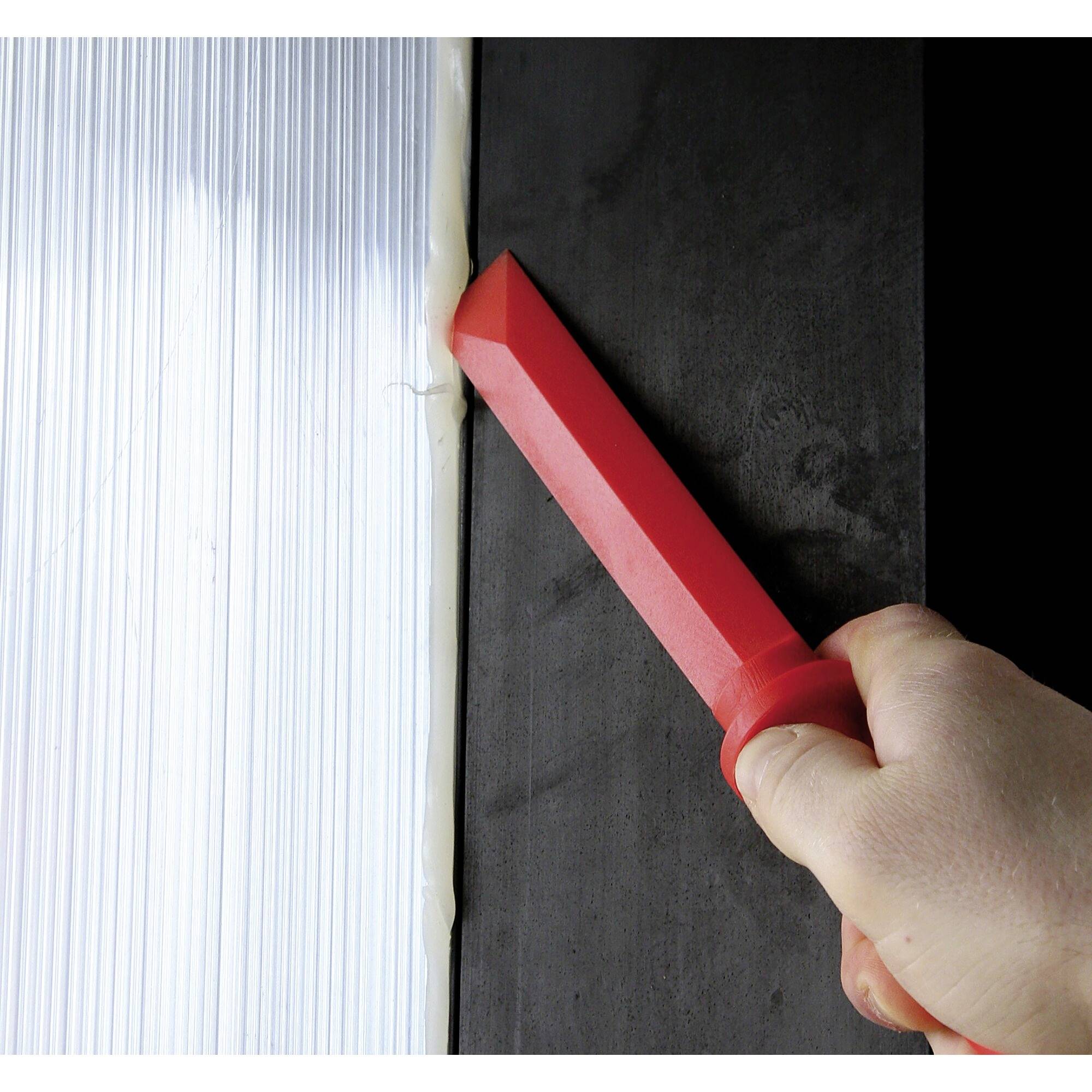 A hand is holding a red tool drawing a white stripe along a black surface, possibly for cutting.