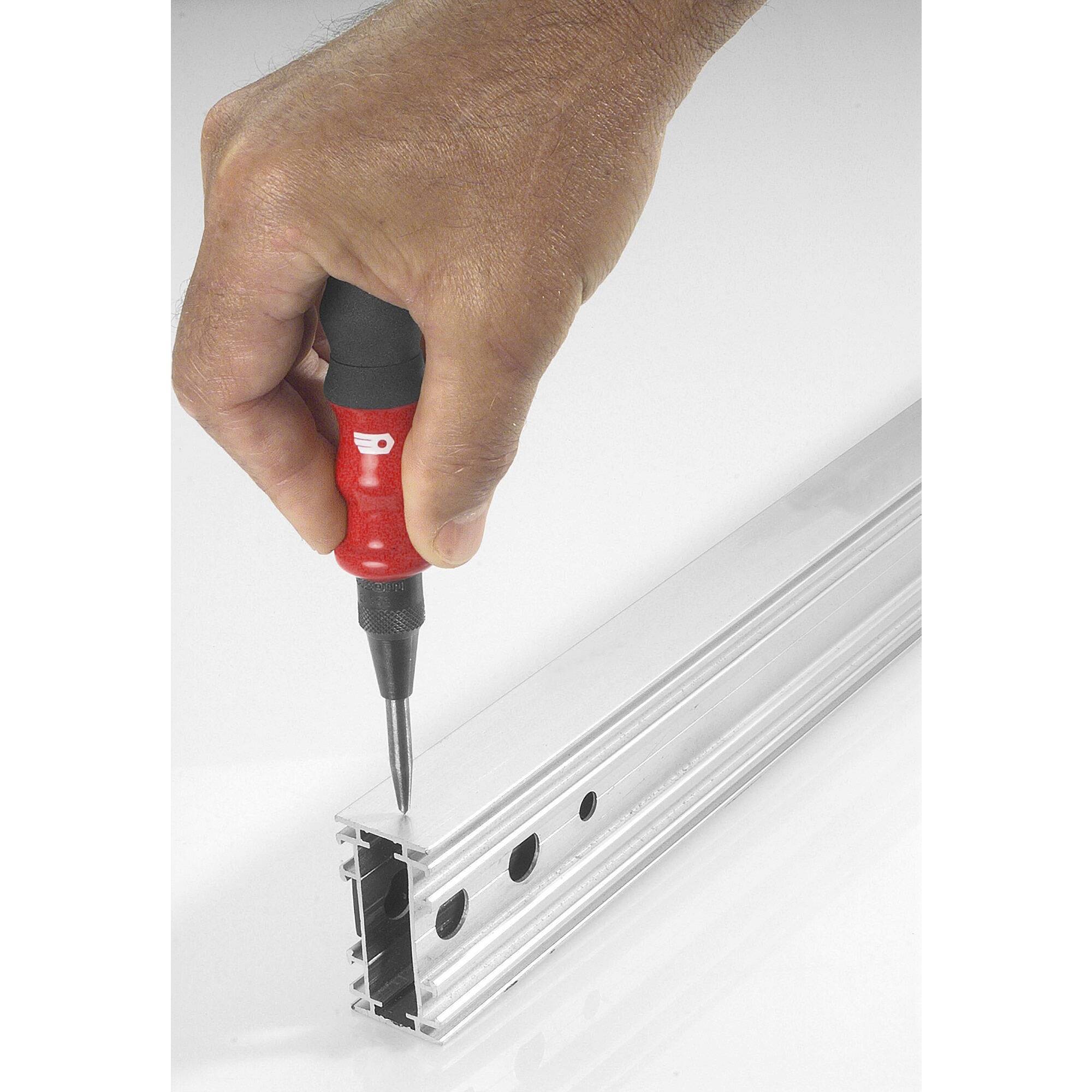 'A hand is holding a screwdriver and pointing it towards a metal profile with holes, presumably for assembly or adjustment.'