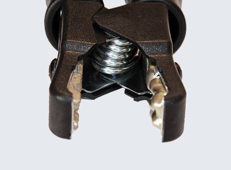 Close-up of a black alligator clip with visible metal teeth and spring, used for connecting to batteries or electrical components.