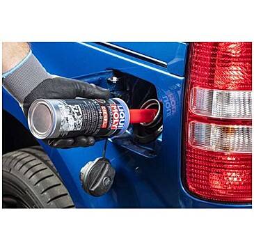 A person is pouring a 'Liqui Moly Diesel' additive bottle into the fuel tank of a blue vehicle, wearing gloves. The fuel cap hangs open.