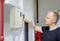 A man unlocks a wall-mounted fuse box with a key. Pipework and a fire extinguisher are visible in the background.