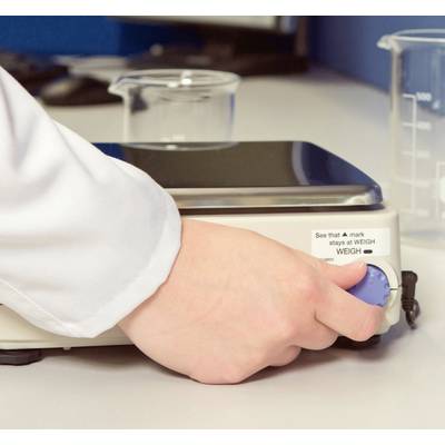 A hand turns the blue button on a laboratory device, most likely a magnetic stirrer, on a table with beakers in the background.