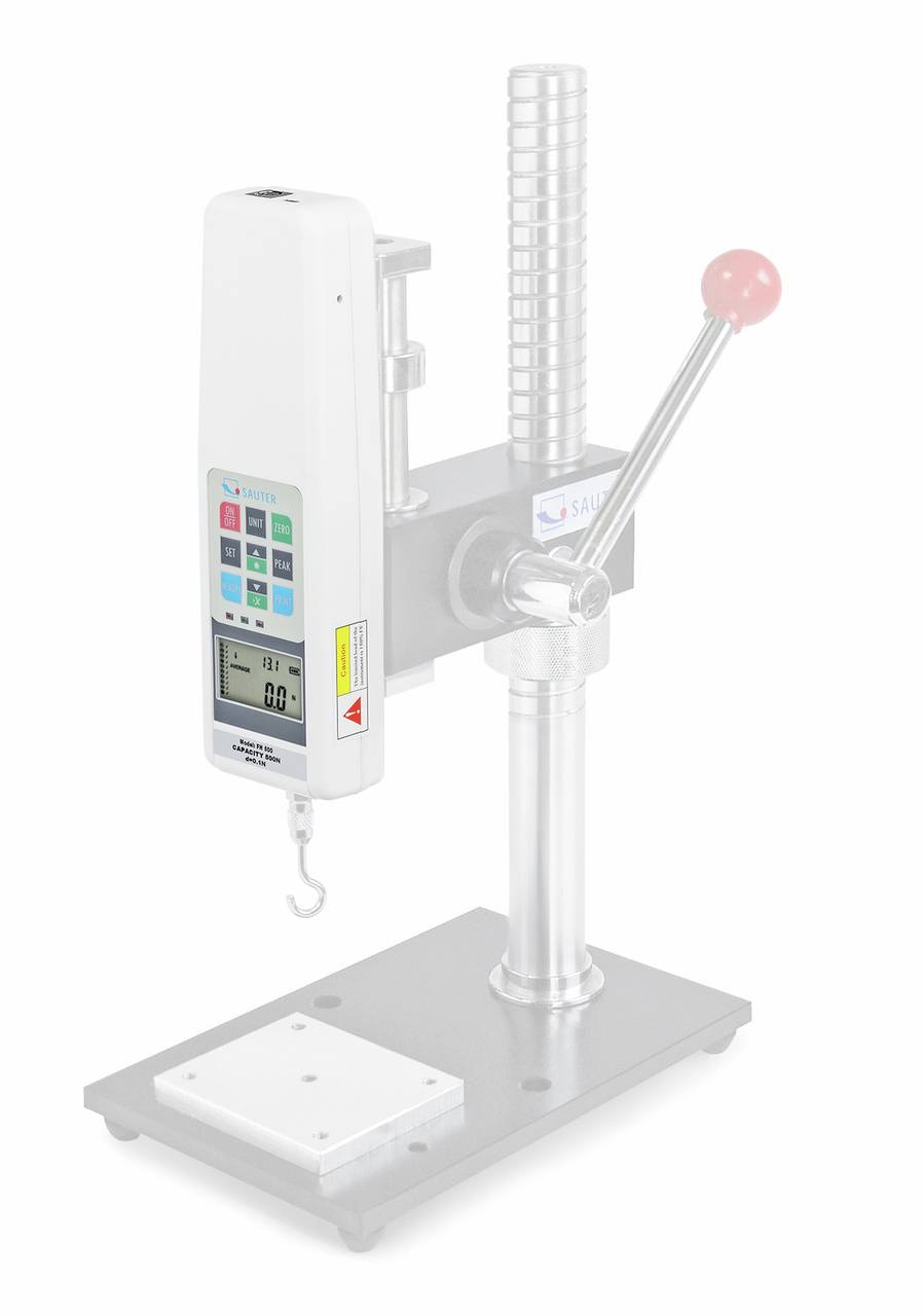A white testing device with a digital display and hook, mounted on a silver stand with a handle.