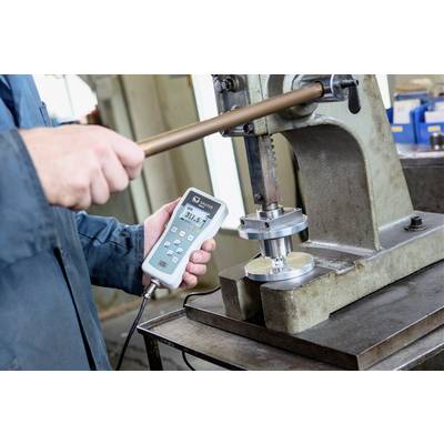 A technician is using a portable hardness testing device on a metal press in a workshop environment.