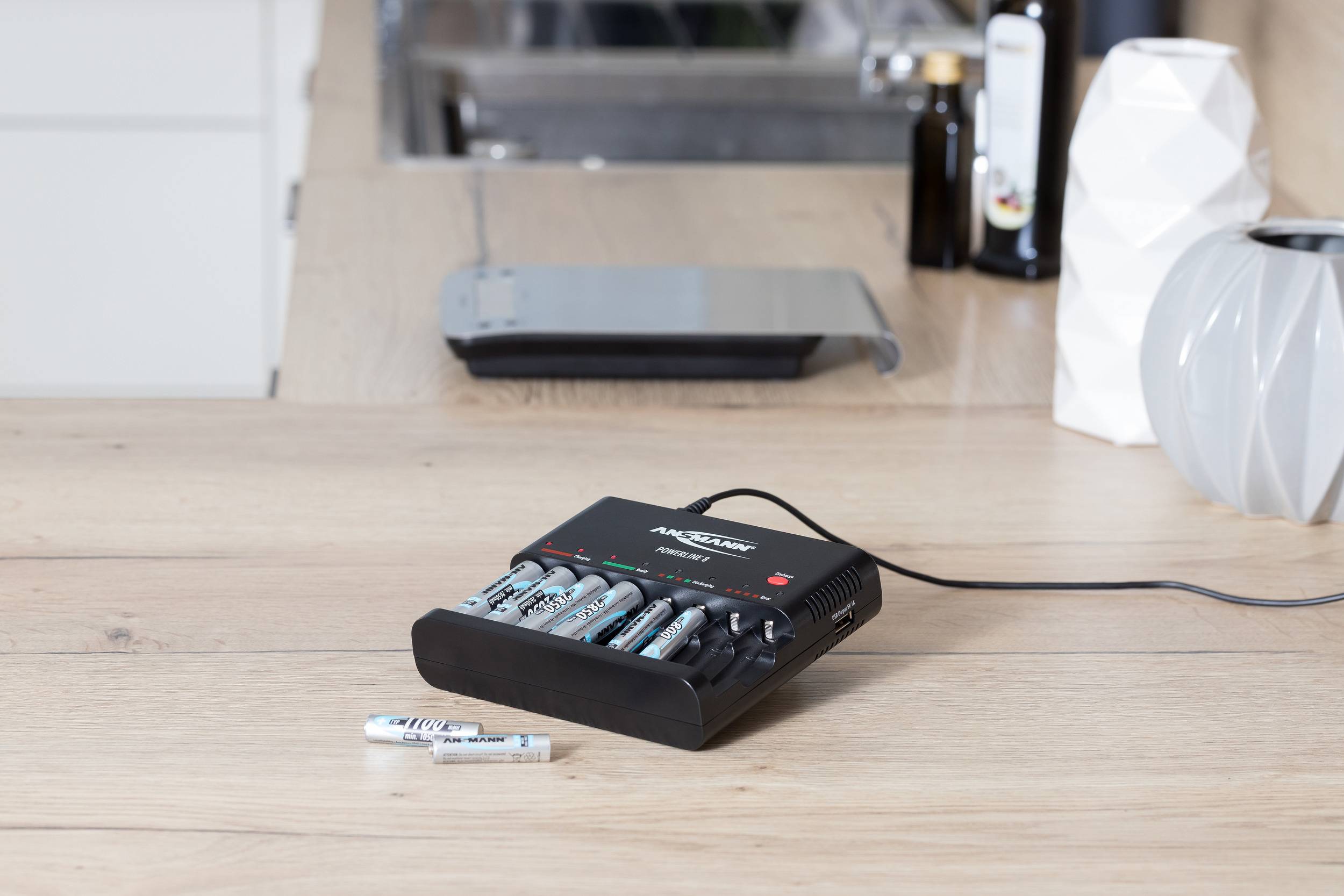 Battery charger for AA batteries on a wooden table, with multiple batteries being charged simultaneously.