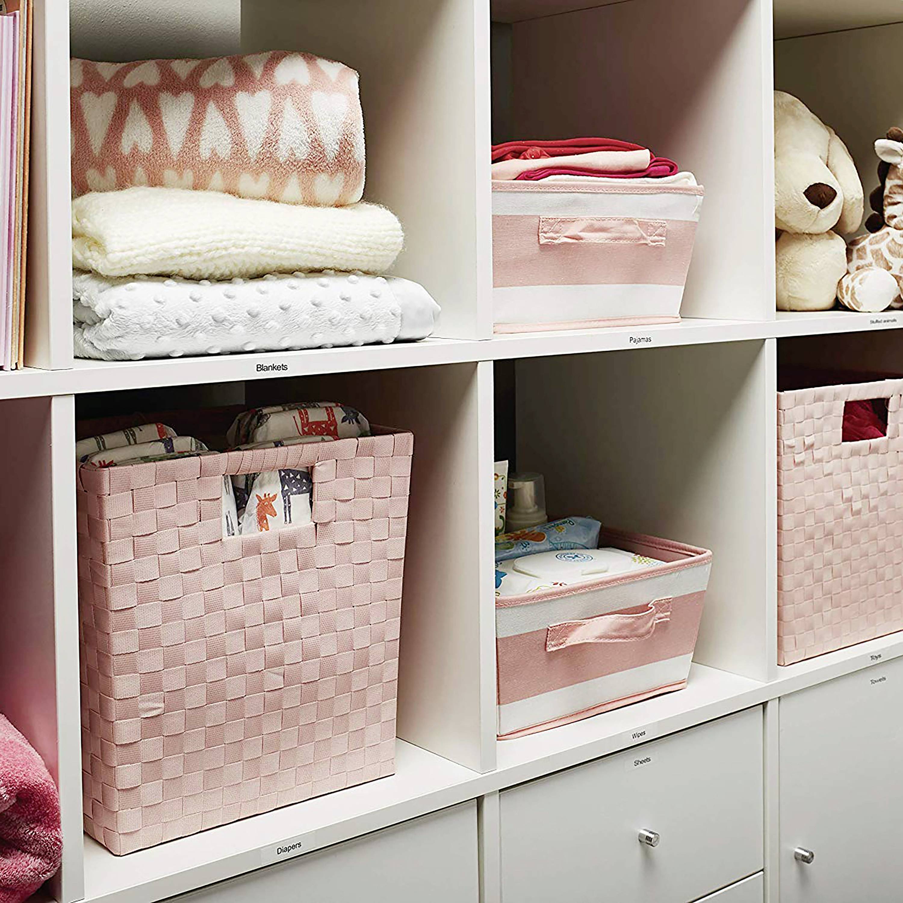 Shelving unit with pink storage baskets and toys. Neatly and decoratively arranged, containing clothing and soft toys.