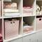 Shelving unit with pink storage baskets and toys. Neatly and decoratively arranged, containing clothing and soft toys.