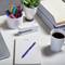 Desk with pens, sticky notes, plants and a cup of coffee. Office supplies are arranged around a laptop.