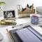 A desk with office items such as a notebook, a mug, pens, a folder and a black and white photograph in a frame.