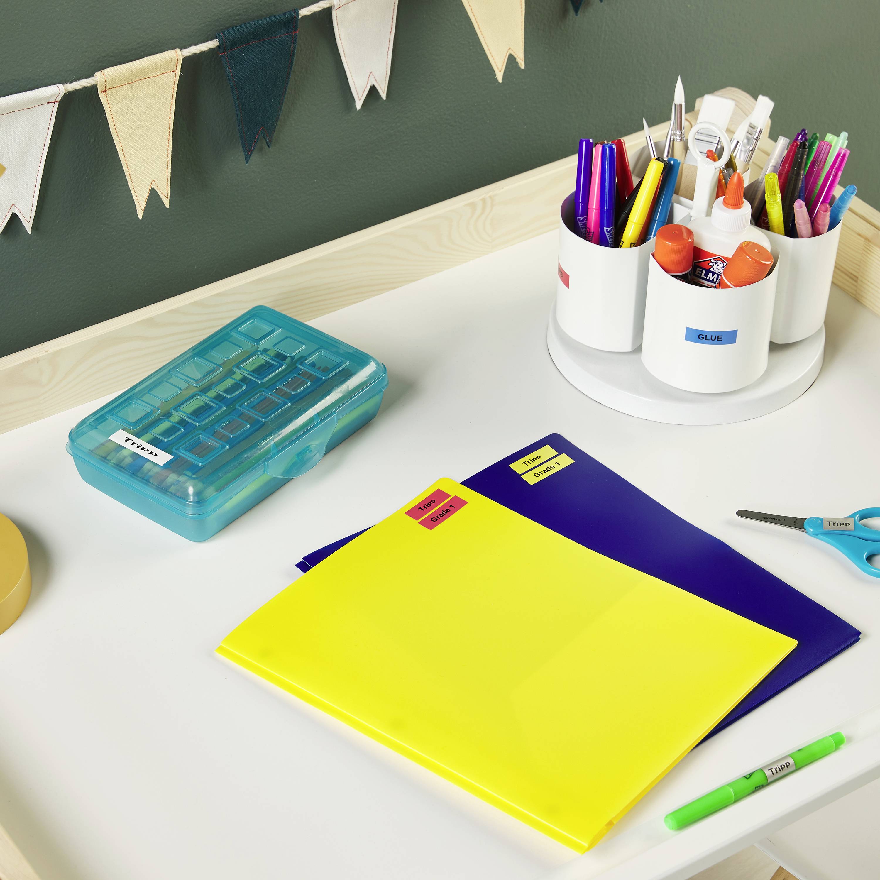 A desk with colourful folders, a pencil holder full of writing materials, a blue box and bunting decorating the wall.