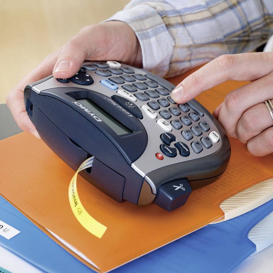 A person is printing a label with a portable label printer onto an orange folder.