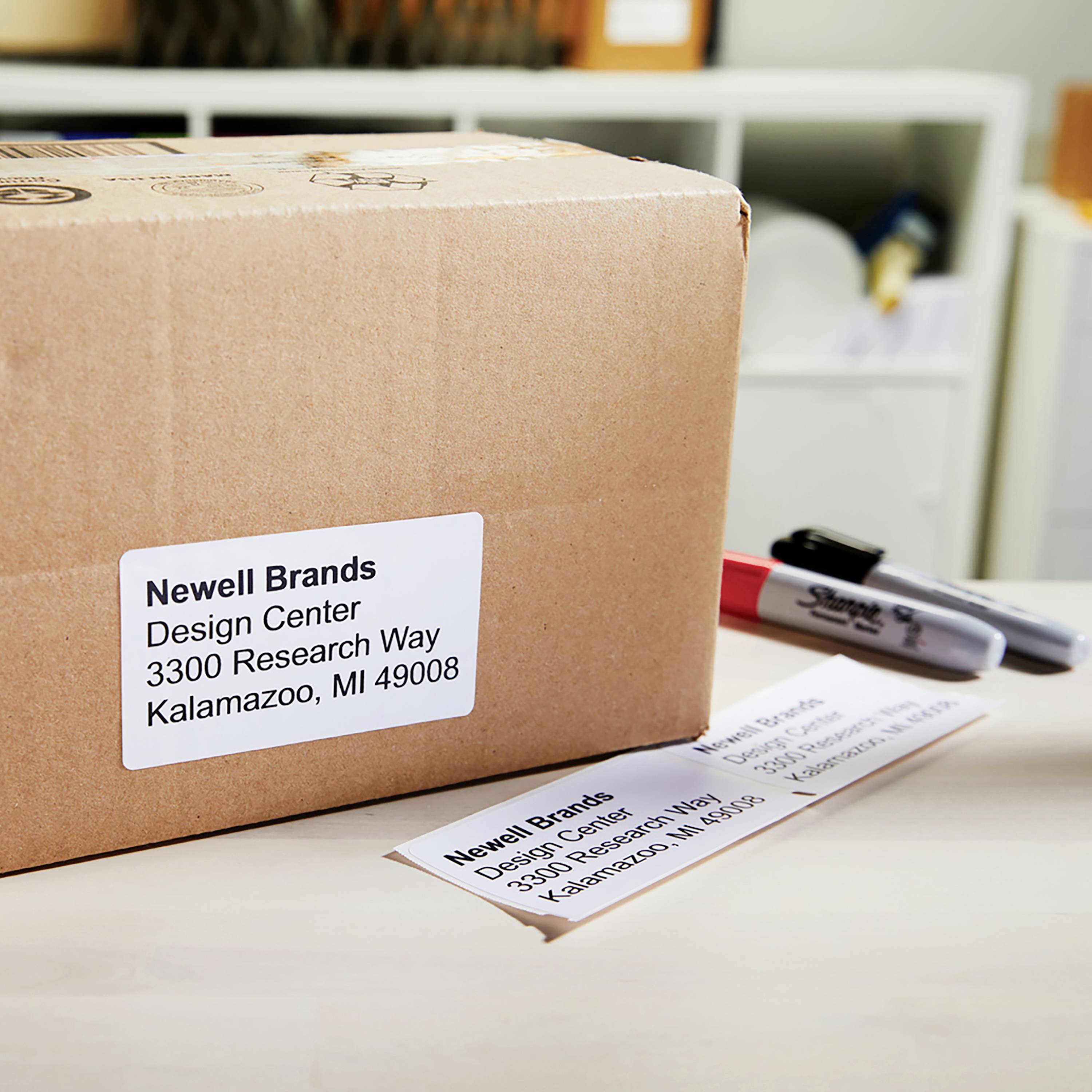 Package with the label 'Newell Brands, Design Centre, 3300 Research Way, Kalamazoo, MI 49008' on a table, with two markers beside it.