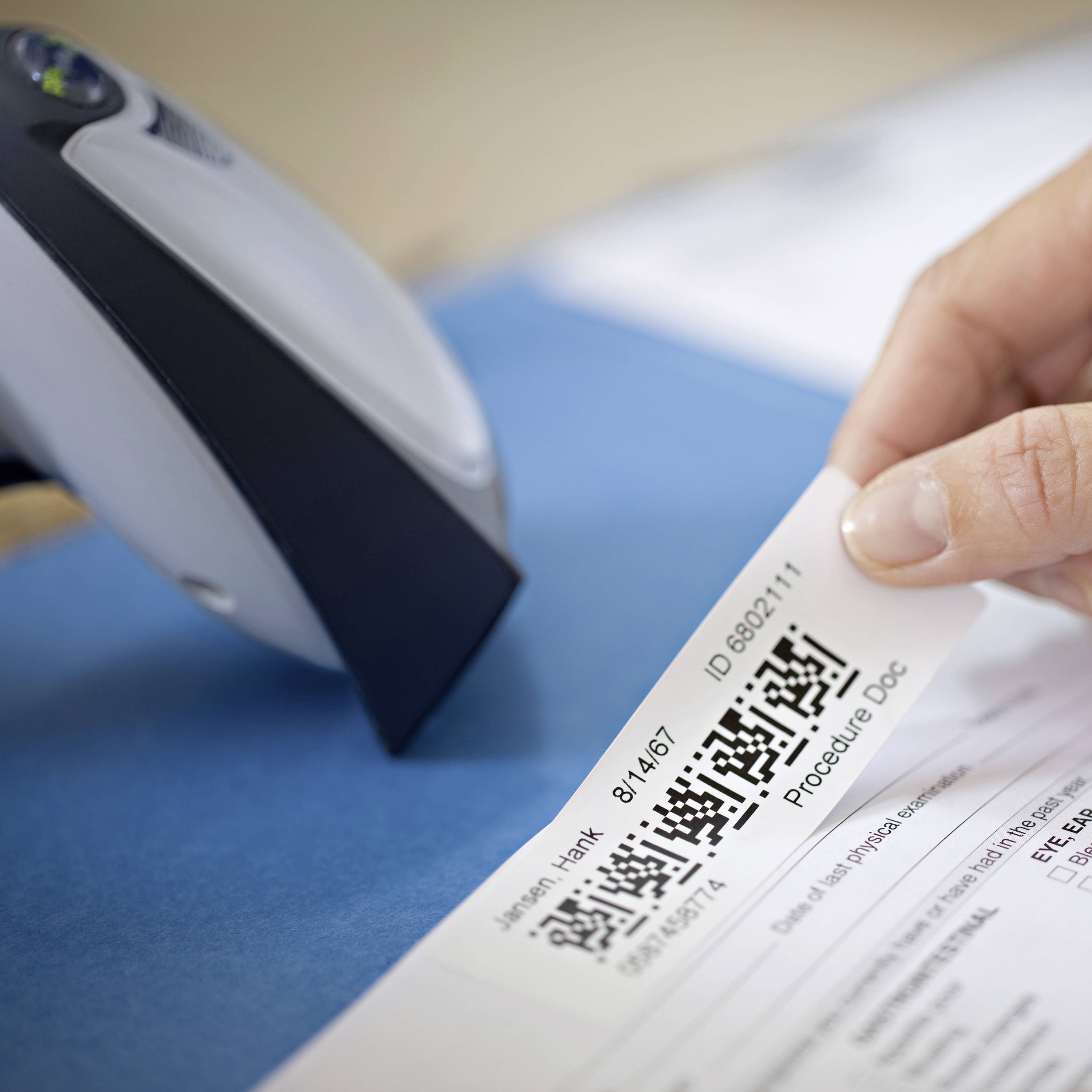 A person is holding a slip of paper with a QR code and text details in front of a card payment terminal at a counter.