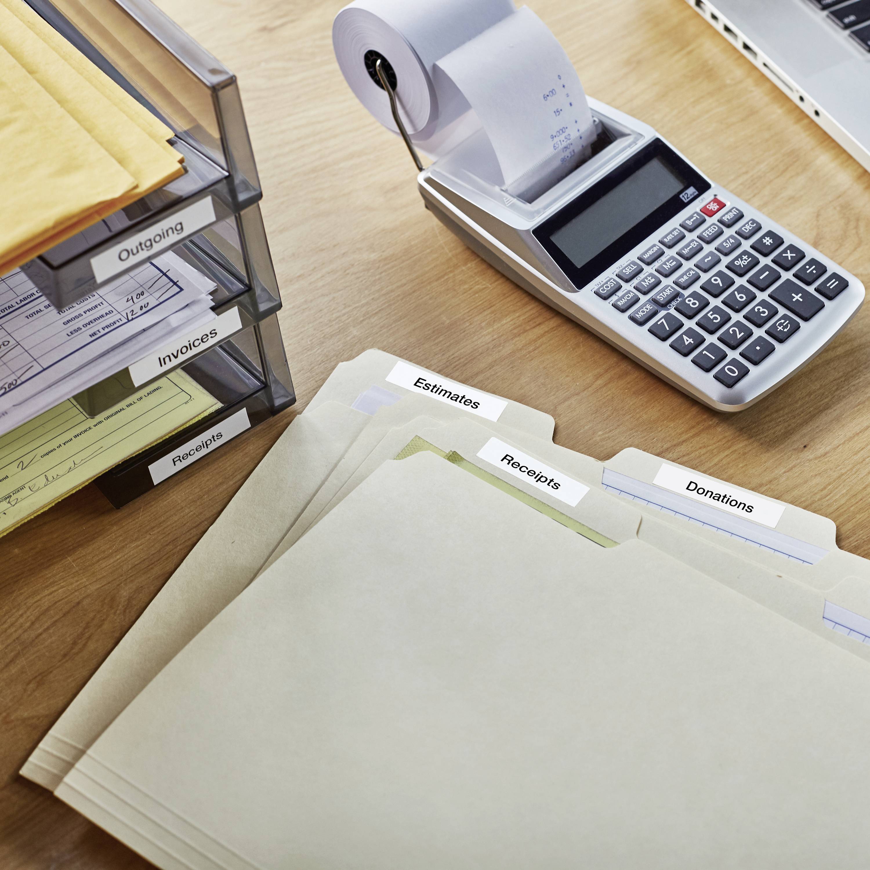 A desk with a stack of folders, including 'Estimates', 'Receipts' and 'Donations'. Beside these sits a calculator with a paper roll.