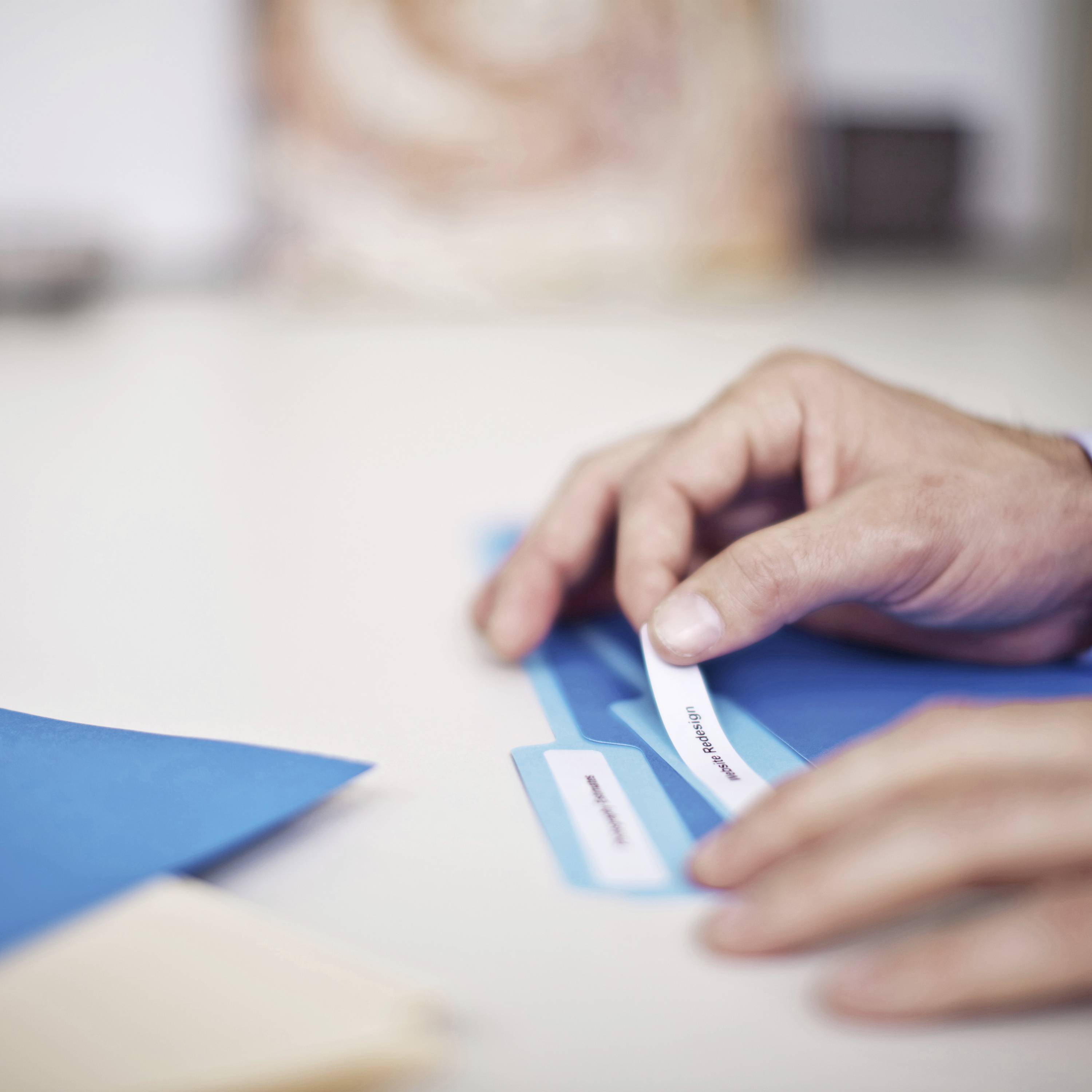 A hand holds a label with the inscription 'management' and places it on a blue folder on a desk.