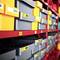 Several plastic boxes in a red shelf, numbered and labelled with coloured tags, in a storage room.