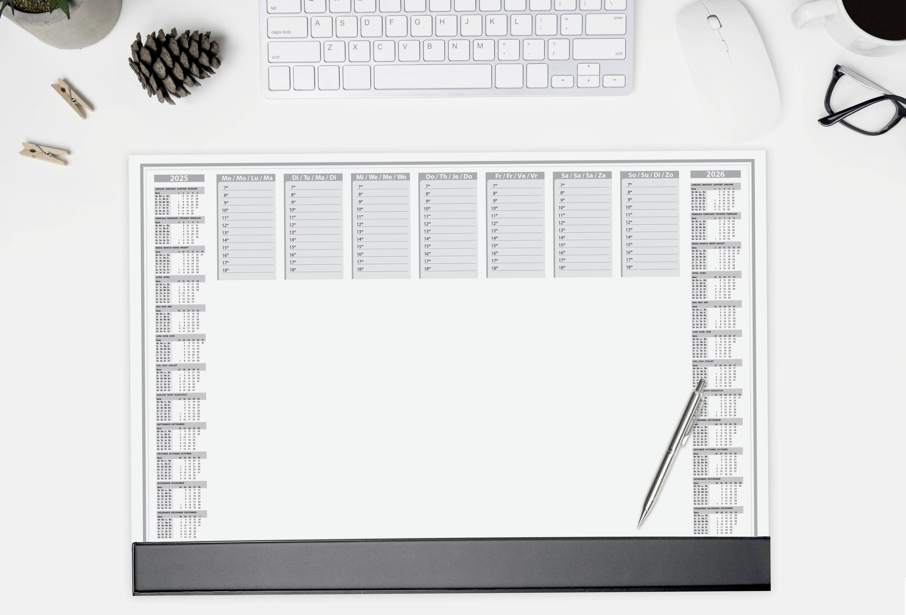 Desk with keyboard, mouse, glasses, coffee cup and paper calendar with a pen lying on it. Used for organising appointments.