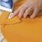 A hand is ironing an orange shirt, attaching a name tag on the inside of the collar.