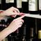 A hand places a red label with the text 'Cabernet' on a wine shelf to mark bottles. Wine bottles are visible in the background.