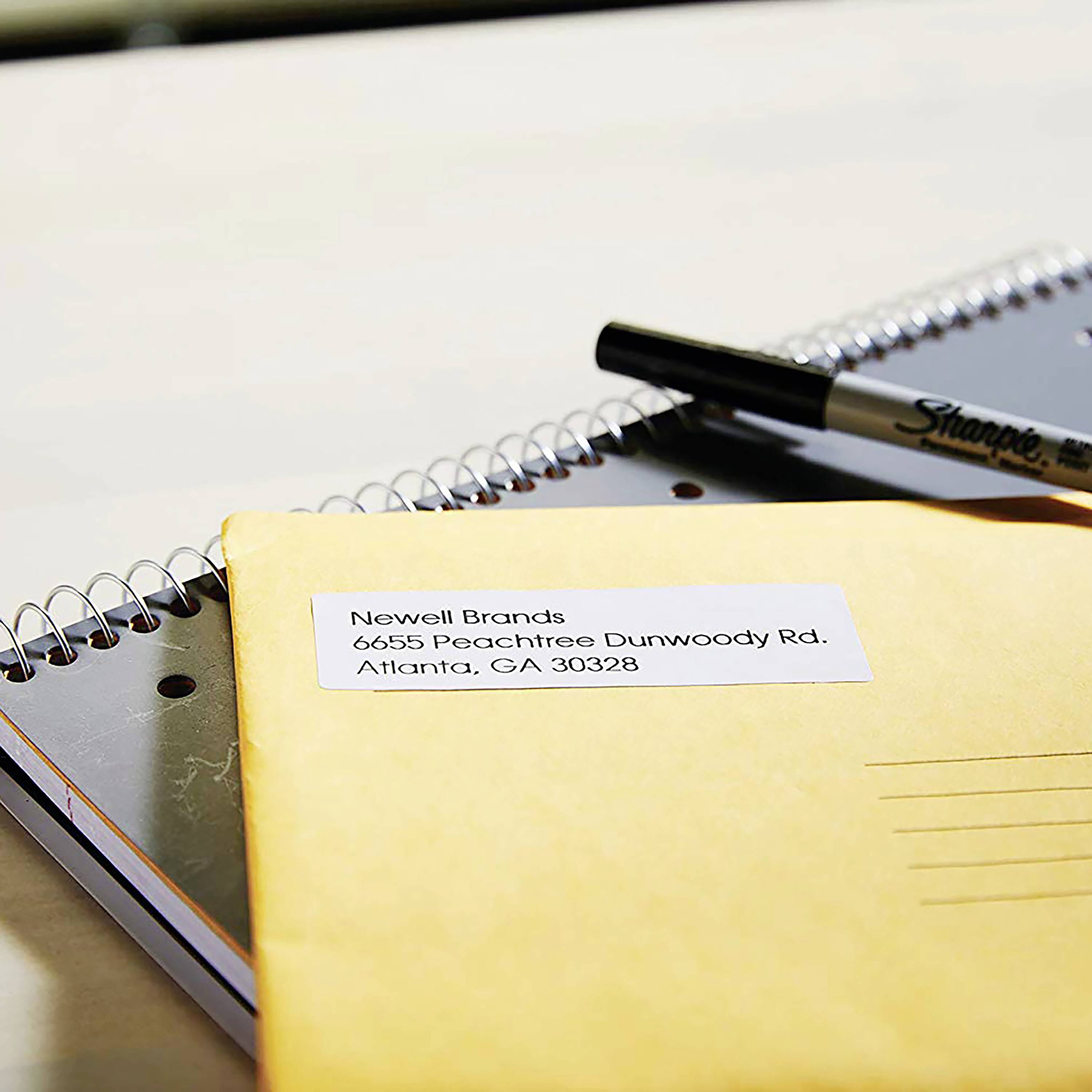 An envelope addressed to 'Newell Brands, 6655 Peachtree Dunwoody Rd., Atlanta, GA 30328', beside a notebook and a pen.