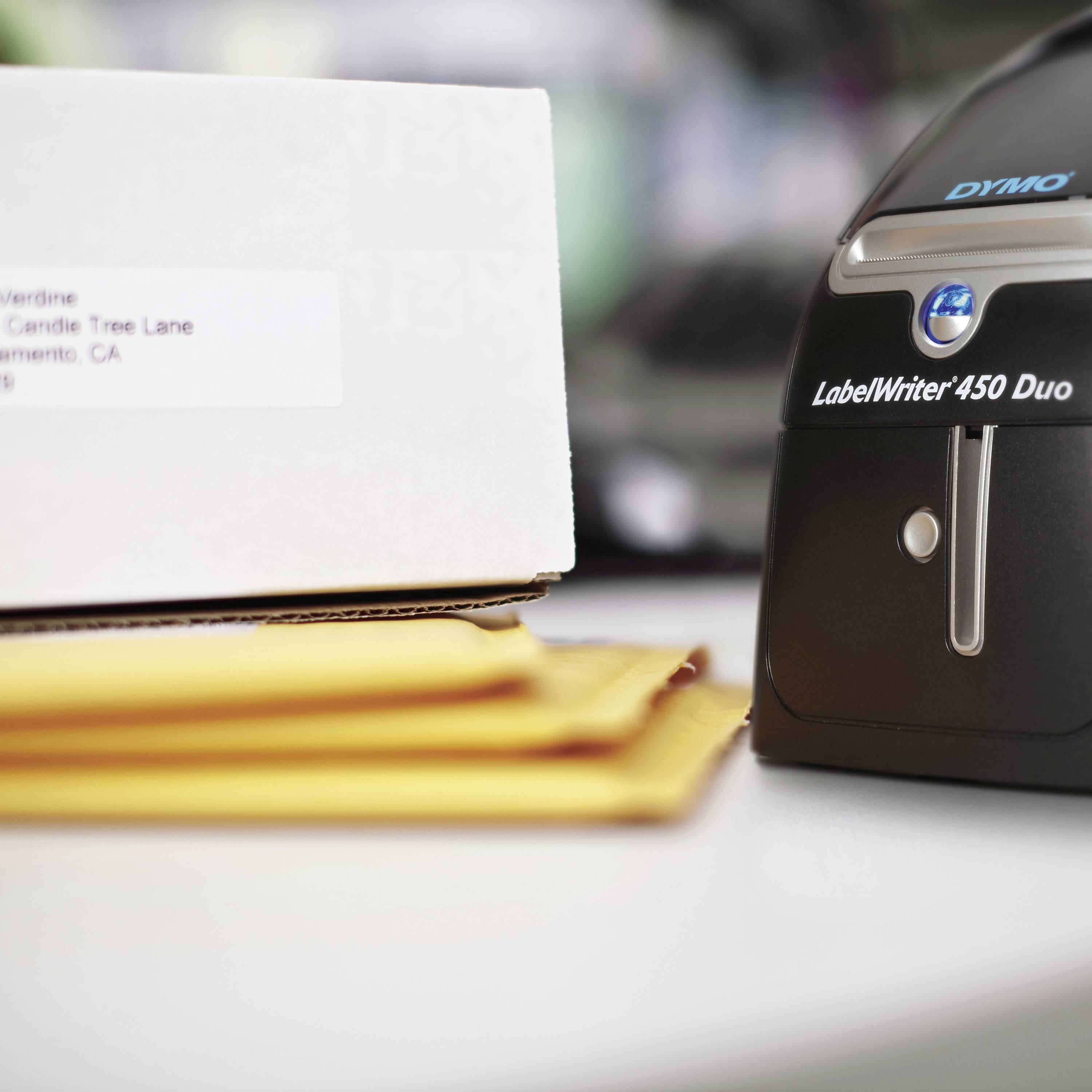 Label printer on a table next to a package with a white label. Focus on the printer.