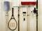 Various tools and a tennis racket are neatly hung on a wooden wall, including a shovel, a rake, a broom, and a hammer.