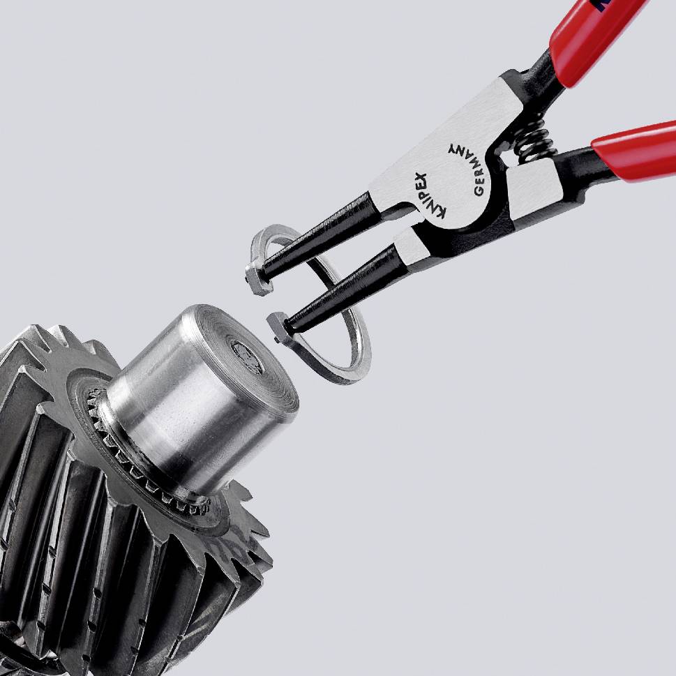 A needle-nose pliers is holding a circlip over a large gear wheel.