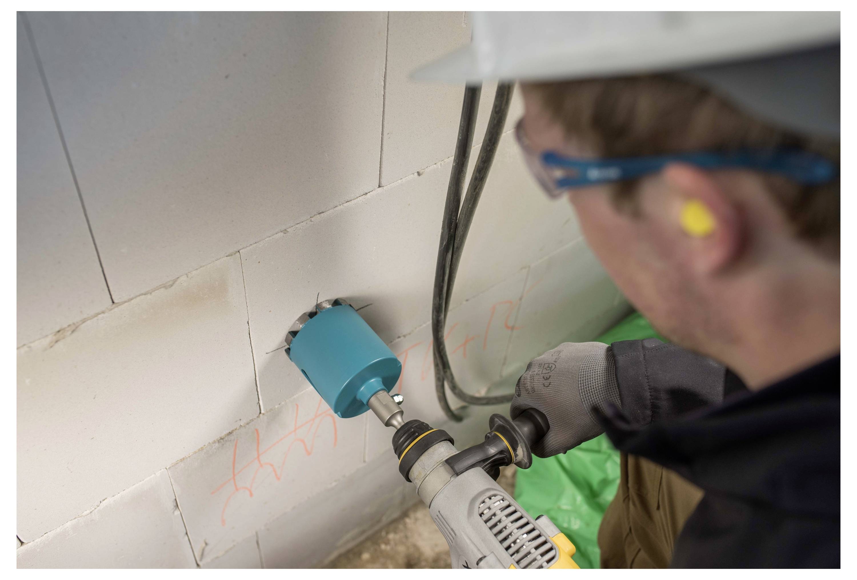 Worker drills into a tiled wall, removing a blue pipe fitting during plumbing or electrical installation.