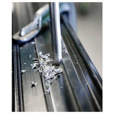 Close-up of a drill bit cutting into a metal surface, with metal shavings scattered around the drilling point.