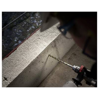A person uses a power drill to bore into a concrete wall near a ledge, with the drill bit touching the surface.