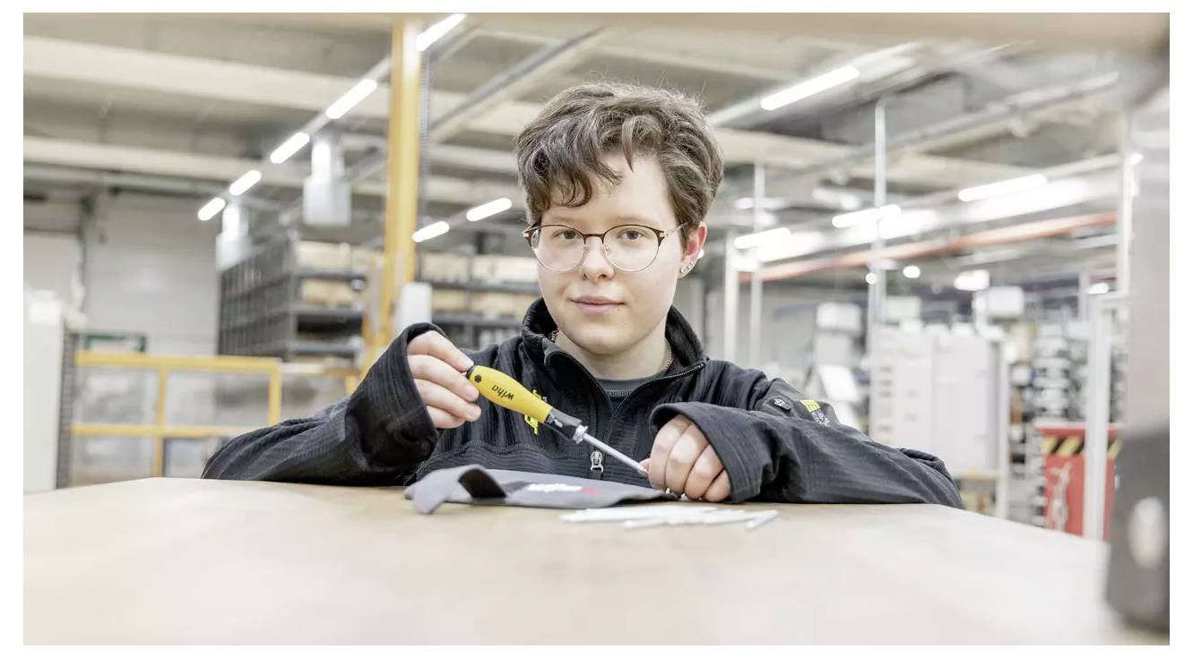 A person using a handheld tool on a fabric piece in an industrial setting, focusing on detailed work.